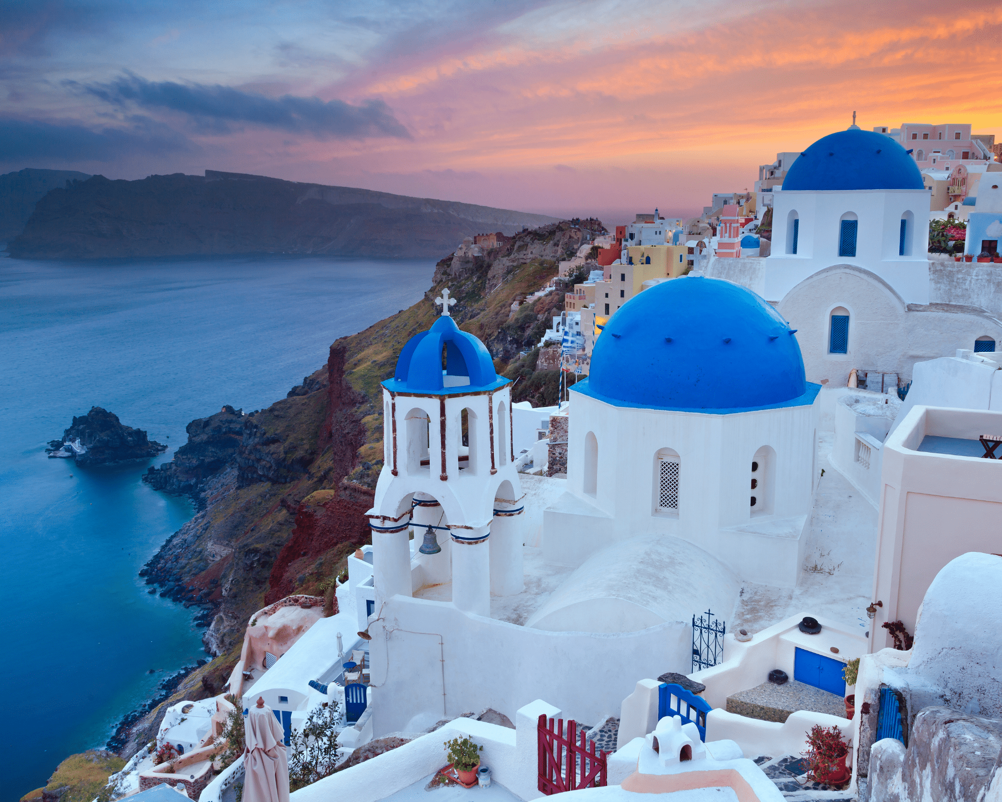 The white wash buildings and blue roofs of Santorini at sunset.